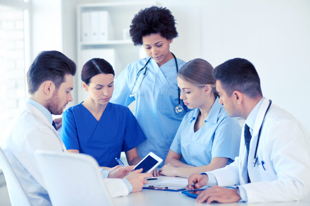 Home health clinicians in an office team huddle reviewing a tablet and visit paperwork
