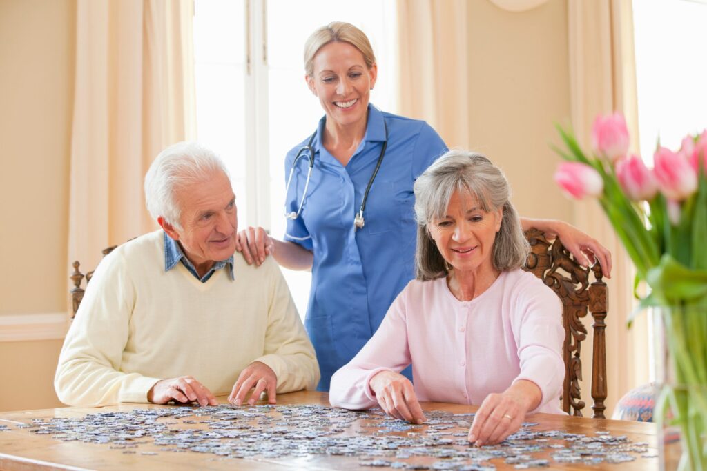 Home caregiver smiling as a senior couple assembles a jigsaw puzzle at the table