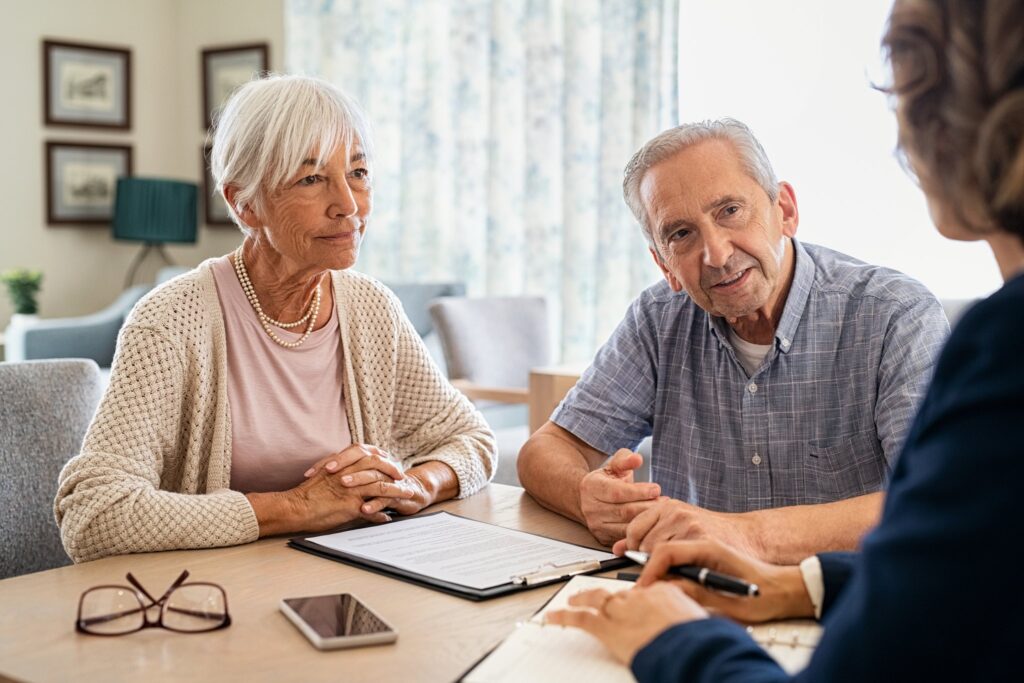 Senior couple reviewing health plan paperwork with an adviser at a table at home