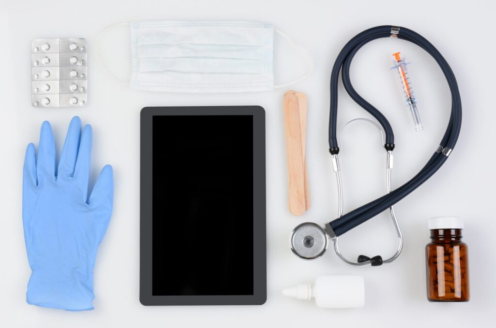 Flat lay of medical supplies including gloves, syringe, mask, stethoscope and a tablet