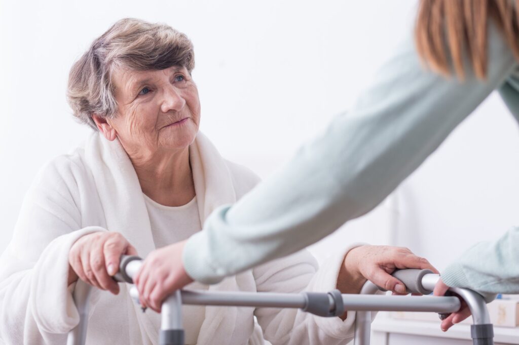Caregiver helping an older woman stand and walk with a walker at home