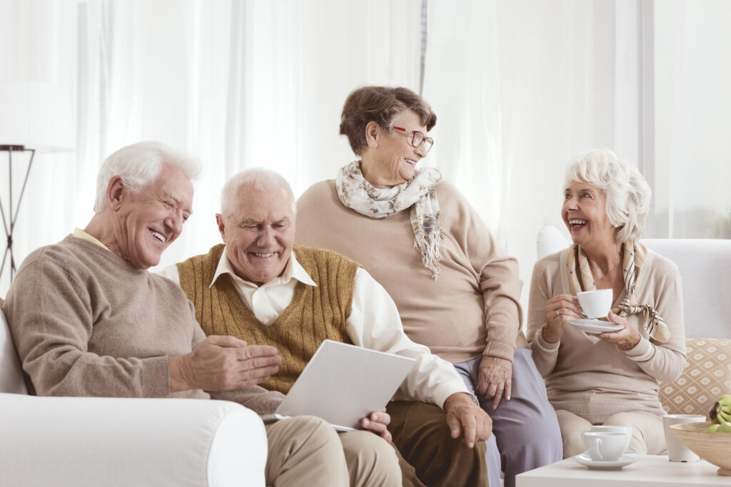 Elderly friends relaxing at a day center, chatting and using a laptop
