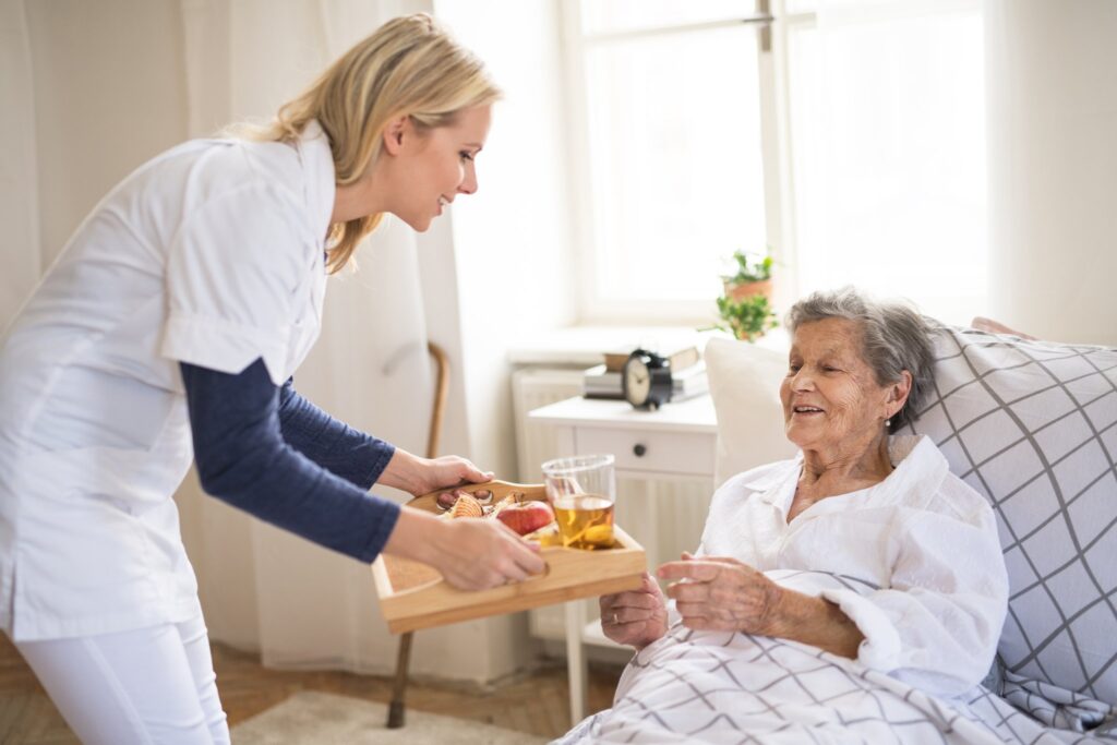 Home care aide bringing a breakfast tray to a senior woman resting in bed at home